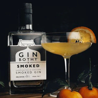 Bottle of Gin Bothy Smoked Gin with a cocktail garnished with an orange slice on a dark background.